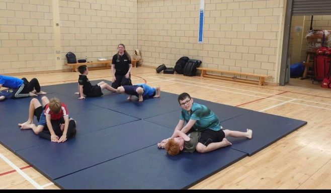 A group of children practising martial arts on mats in a gym.