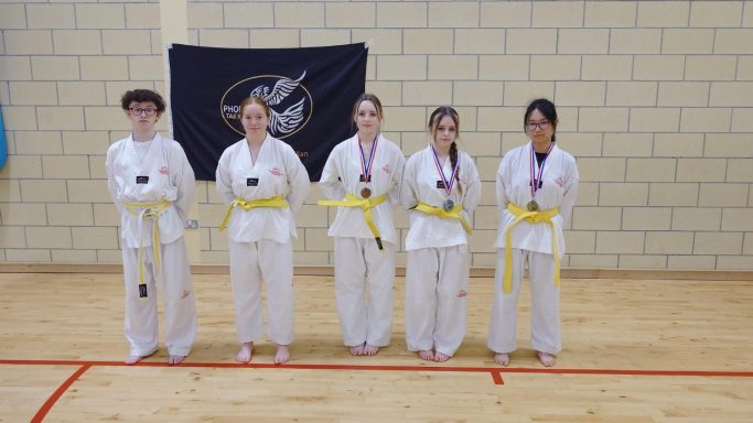 Five martial artists in white uniforms and yellow belts, all wearing medals, standing together.