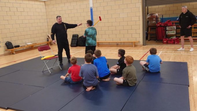 A coach demonstrates techniques to a group of children during a gym class.