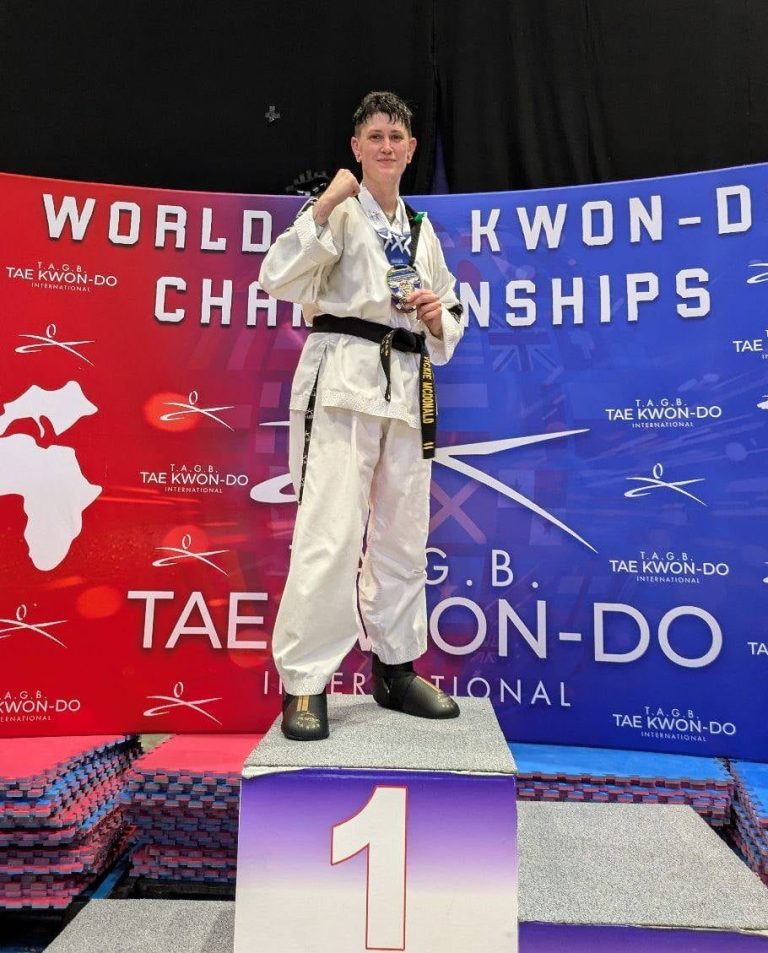 A martial artist in a white gi stands on a podium, holding a medal at a championship event.