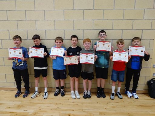 A group of eight boys holding certificates, standing against a wall.